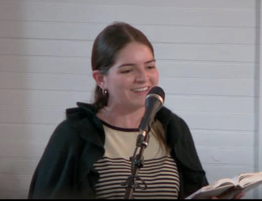 A young woman singing from a hymnal at the microphone